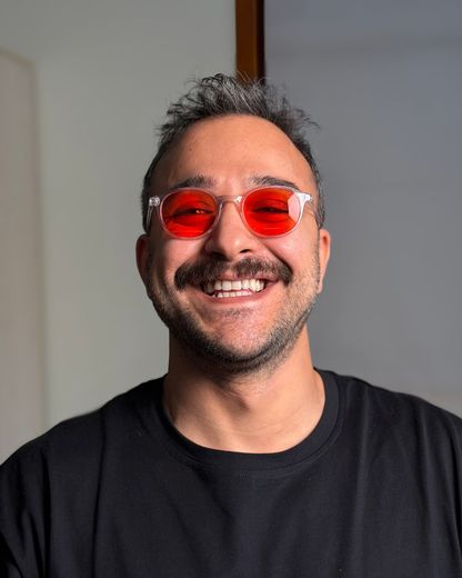 Dr. Can Çiftçi, turuncu camlı gözlüğüyle gülümsüyor